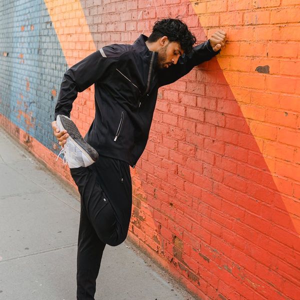 Person stretching energetically in front of a brick-red wall.